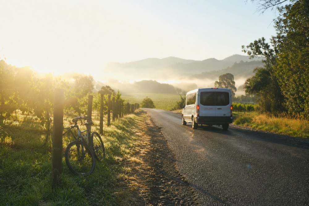 A morning departure scene with a tour vehicle on a valley road between vineyards